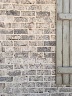 a cat sitting on the ground next to a brick wall with a wooden door and window