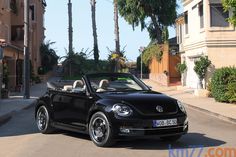 a black convertible car driving down a street next to tall buildings and palm trees in the background