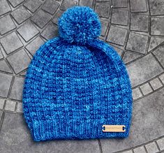 a blue knitted beanie with a tag on the front sitting on a cobblestone floor