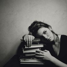 black and white photograph of a woman leaning on stack of books with her hand on top of the book