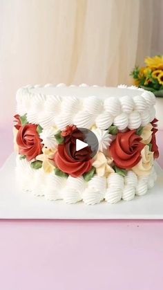 a white cake with red and yellow flowers sitting on top of a pink tablecloth