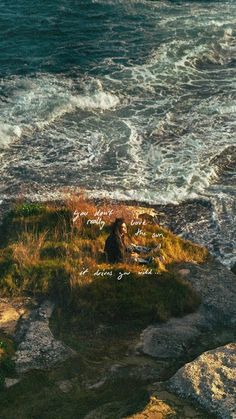 a person sitting on top of a rock next to the ocean