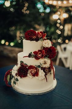 a white wedding cake with red and white flowers on the top is sitting on a table