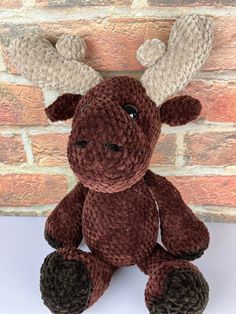 a crocheted moose stuffed animal sitting in front of a brick wall and wearing antlers