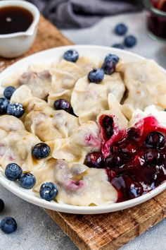 a bowl filled with dumplings and blueberries on top of a wooden cutting board