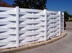 a white fence is shown in front of a tree and some bushes on the side of the road