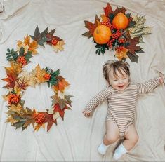 a baby laying on a blanket next to two wreaths with oranges and leaves