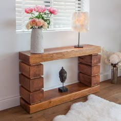 a vase with flowers sitting on top of a wooden shelf next to a lamp and window