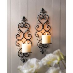 two wall sconces with candles on them in front of a white flower vase