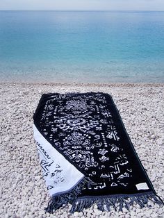 a black and white blanket sitting on top of a sandy beach next to the ocean