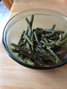 a glass bowl filled with green beans on top of a wooden table