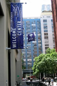 there are people walking on the sidewalk in front of some tall buildings and one has a blue banner hanging from it