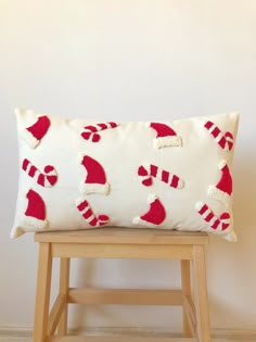 a white pillow with red santa hats and candy canes on it sitting on a wooden stool