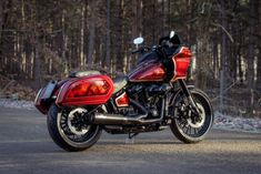 a red and black motorcycle parked on the side of a road in front of some trees