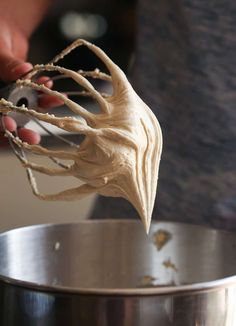 a hand holding a whisk over a metal bowl