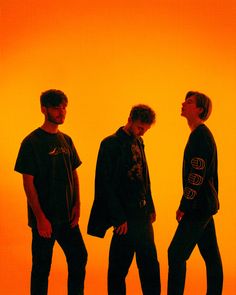 three young men standing next to each other in front of an orange background with the sun behind them