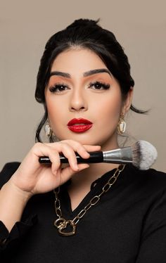 a woman with red lipstick holding a makeup brush in her hand and looking at the camera