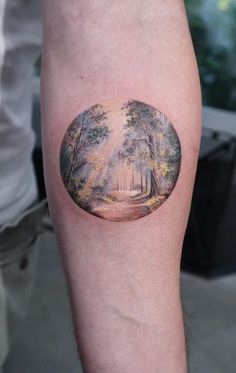 a person with a tattoo on their arm has a forest scene in the middle of it