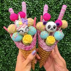 someone holding two ice cream cones with panda bears and unicorns on them in front of a hedge