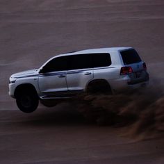 a white truck driving down a dirt road in the middle of the desert with dust coming from its tires