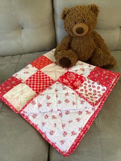 a teddy bear sitting on the couch next to a patchwork blanket that is red and white