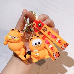 a person holding three key chains with cartoon characters on them, in front of a white background