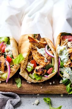 three pita breads filled with chicken, lettuce and tomato salad on a cutting board