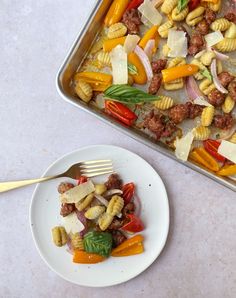 a white plate topped with pasta and veggies next to a pan filled with meat