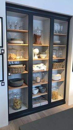 an open cabinet with glass doors and shelves filled with plates, bowls and other items