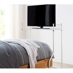 a flat screen tv sitting on top of a metal stand next to a bed in a bedroom