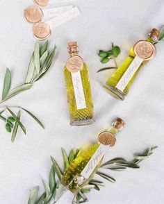 three small bottles filled with green liquid next to some leaves and pennets on a white table cloth