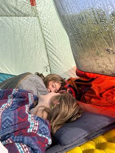 two people laying in a tent sleeping on the ground next to each other with their eyes closed