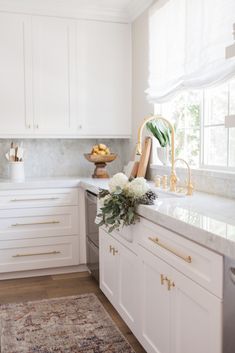 a kitchen with white cabinets and marble counter tops, gold accents on the faucet