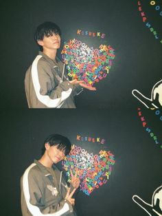 a man holding up a heart made out of letters and numbers in front of a black background