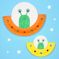 two paper plates with different designs on them and one has a smiling green insect sitting on the moon