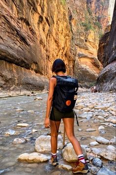 a woman standing on rocks in the middle of a river with a backpack over her shoulder