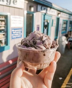 someone is holding up an ice cream sundae in front of a train station platform