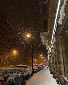 a snowy street with cars parked on the side and people walking down the sidewalk at night