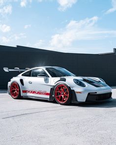 a white sports car with red rims parked in front of a black building on a sunny day