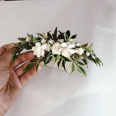 a hand holding a hair comb with white flowers and green leaves on the top of it