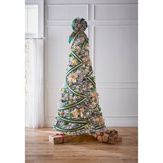 a decorated christmas tree with presents on the floor in front of a white wall and window