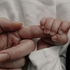 a close up of a person holding a baby's hand with both hands on top of it