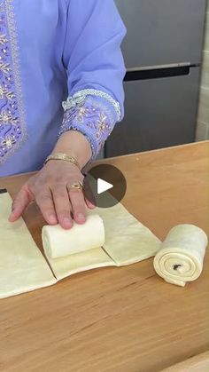 a woman is rolling out dough on top of a wooden table with rolled up rolls