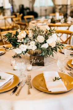 a centerpiece with white flowers and greenery sits on top of a gold plate