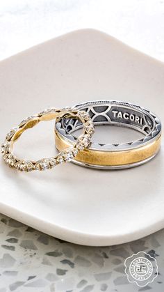 two gold and silver wedding rings on a white plate with the word tacori written in cursive writing