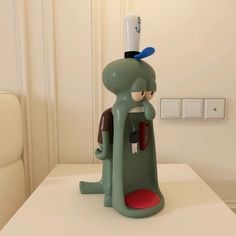 a green cartoon character sitting on top of a white table next to a light switch