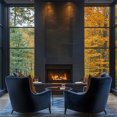 A serene lounge featuring two oversized navy velvet chairs positioned in front of a sleek, modern fireplace. The floor-to-ceiling windows reveal a breathtaking view of vibrant autumn trees, adding warmth and natural beauty to the space. The combination of rich fabrics and clean lines creates a perfect balance between comfort and style. Fall View, Cozy Interiors, Colors Of Autumn, Home Luxury, Fall Inspiration