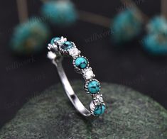 a turquoise and white diamond ring on top of a rock with other jewelry items in the background