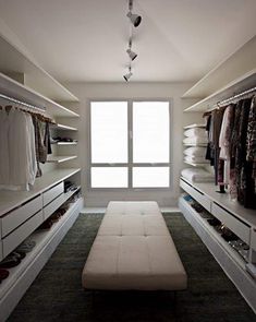 a walk in closet with white shelves and drawers