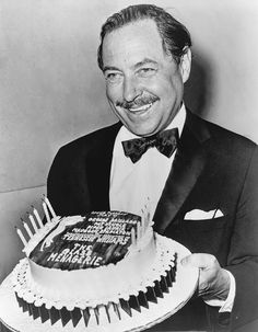 a man in a tuxedo holding a birthday cake